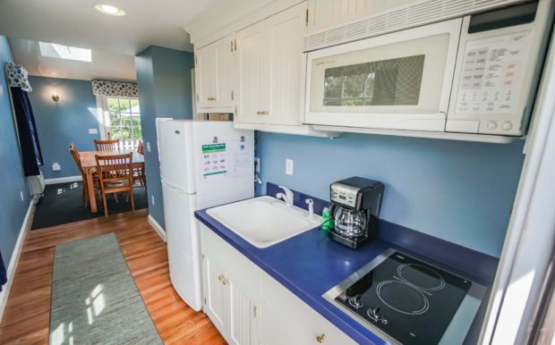 Photo of kitchen, with refrigerator, sink, stovetop, microwave and white cabinets.